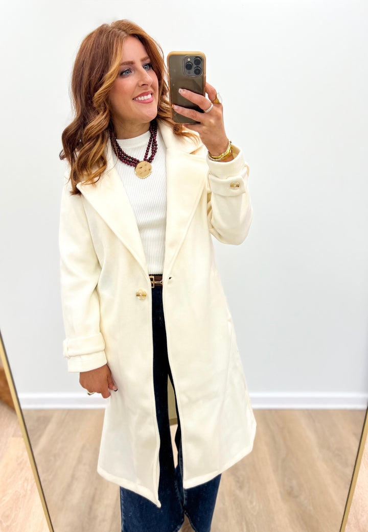 Cream longline coat with notch collar, button front, and side pockets