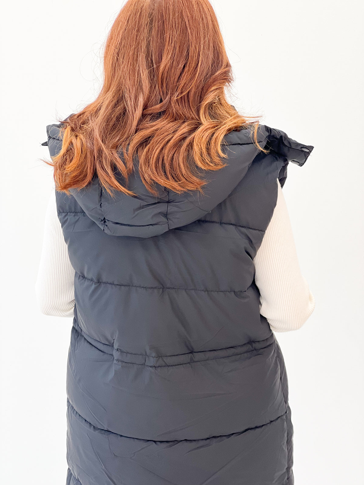 Back view of longline quilted puffer vest with hooded collar and horizontal quilting