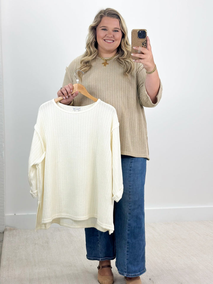Off-white knit top with 3/4 folded sleeves, round neckline, ribbed fabric (laid out)