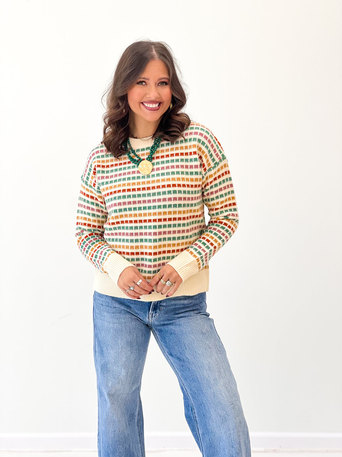 Multi-color striped sweater with gold button pendant at crew neckline, long sleeves
