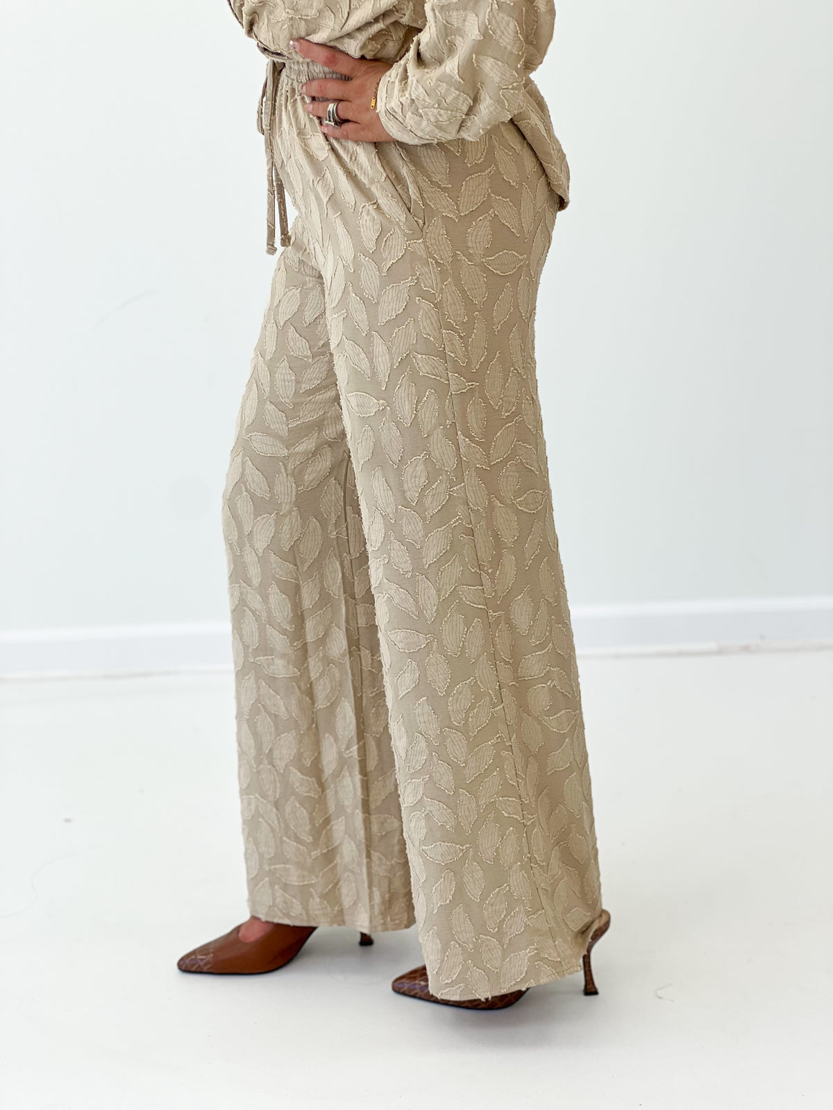 Taupe elastic tie-waist pants with leaf pattern and long wide legs.