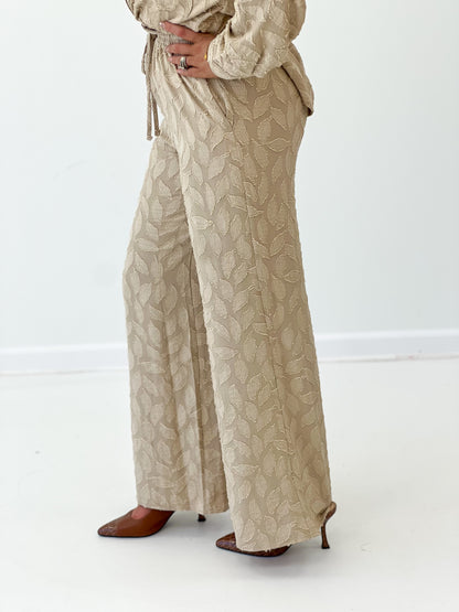 Taupe elastic tie-waist pants with leaf pattern and long wide legs.