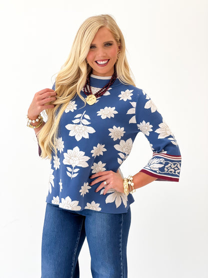 Blue mock neck knit sweater with white floral print and red-trimmed cuffs