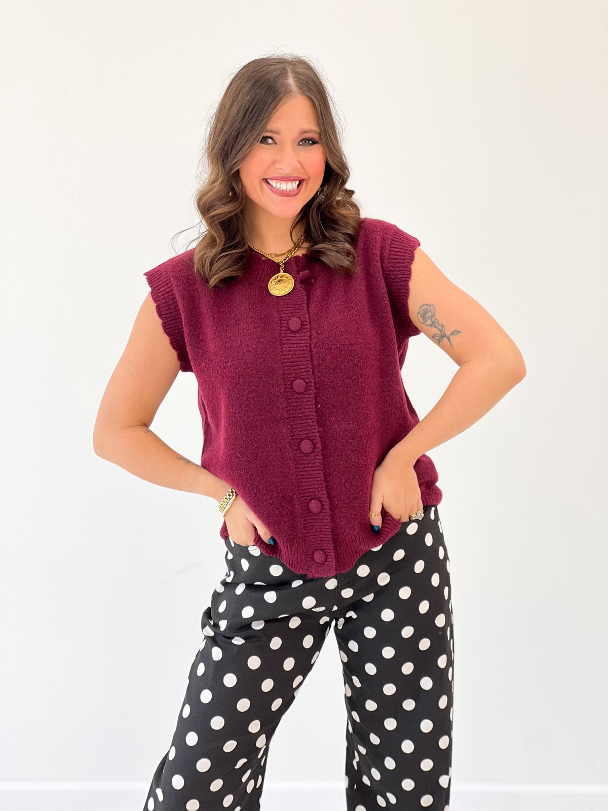 Burgundy ribbed sleeveless sweater vest with scalloped trim and gold round buttons