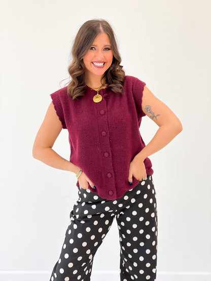Burgundy ribbed sleeveless sweater vest with scalloped trim and gold round buttons