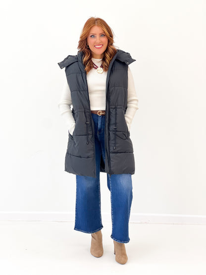 Black longline quilted puffer vest with hooded collar and front snap details