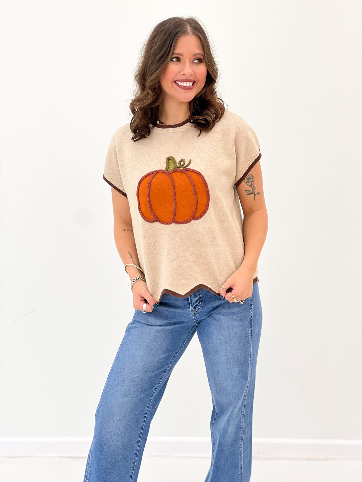 Light taupe short-sleeve sweater with orange pumpkin graphic and scalloped bottom hem