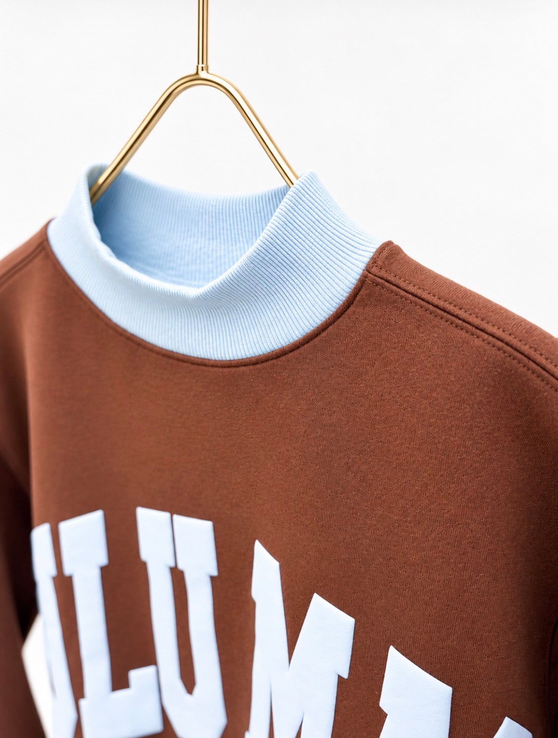 Brown sweatshirt close-up with light blue mock neck and partial white 'LuLu Mac' print
