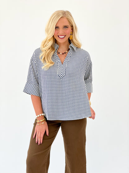 Blue and white gingham short-sleeve V-neck top, draped shoulders and loose fit.