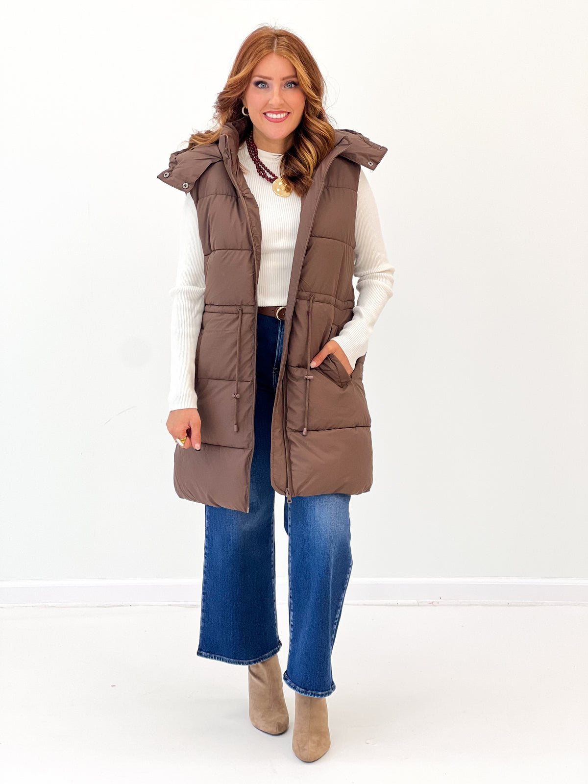 Brown longline quilted puffer vest with button front, hooded collar, and pockets