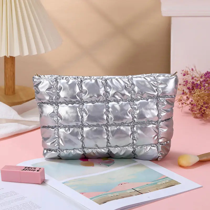 Small travel makeup bag in silver with a quilted, padded finish and zip closure.