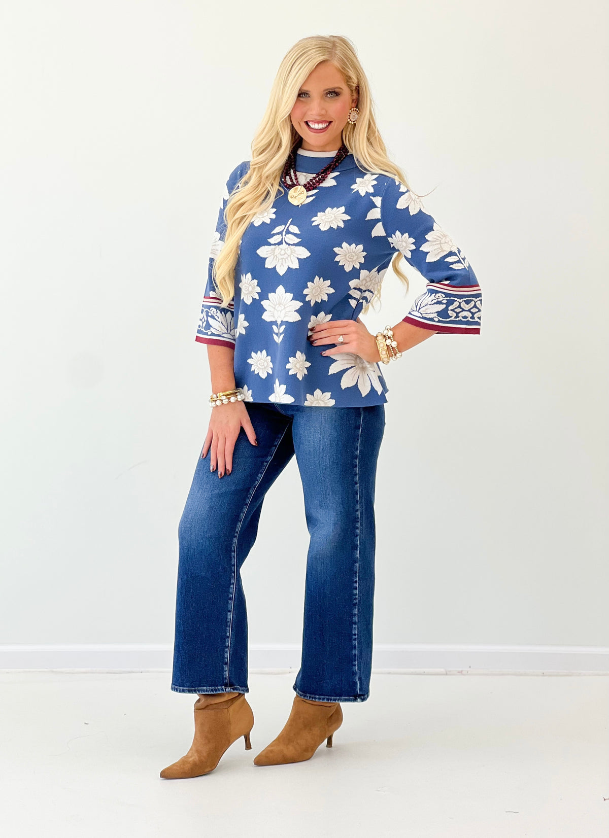 Blue mock neck knit sweater with white floral print and red border on sleeves
