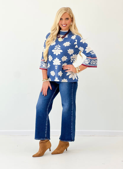 Blue mock neck knit sweater with white floral print and red border on sleeves