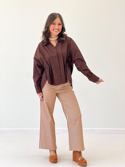 Brown V-neck pleated-waist blouse with long sleeves and button placket details.