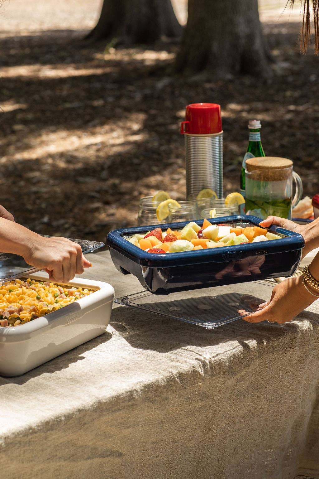 Navy blue foil pan carrier on outdoor table with hands serving food