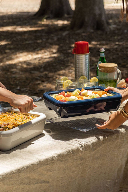 Navy blue foil pan carrier on outdoor table with hands serving food