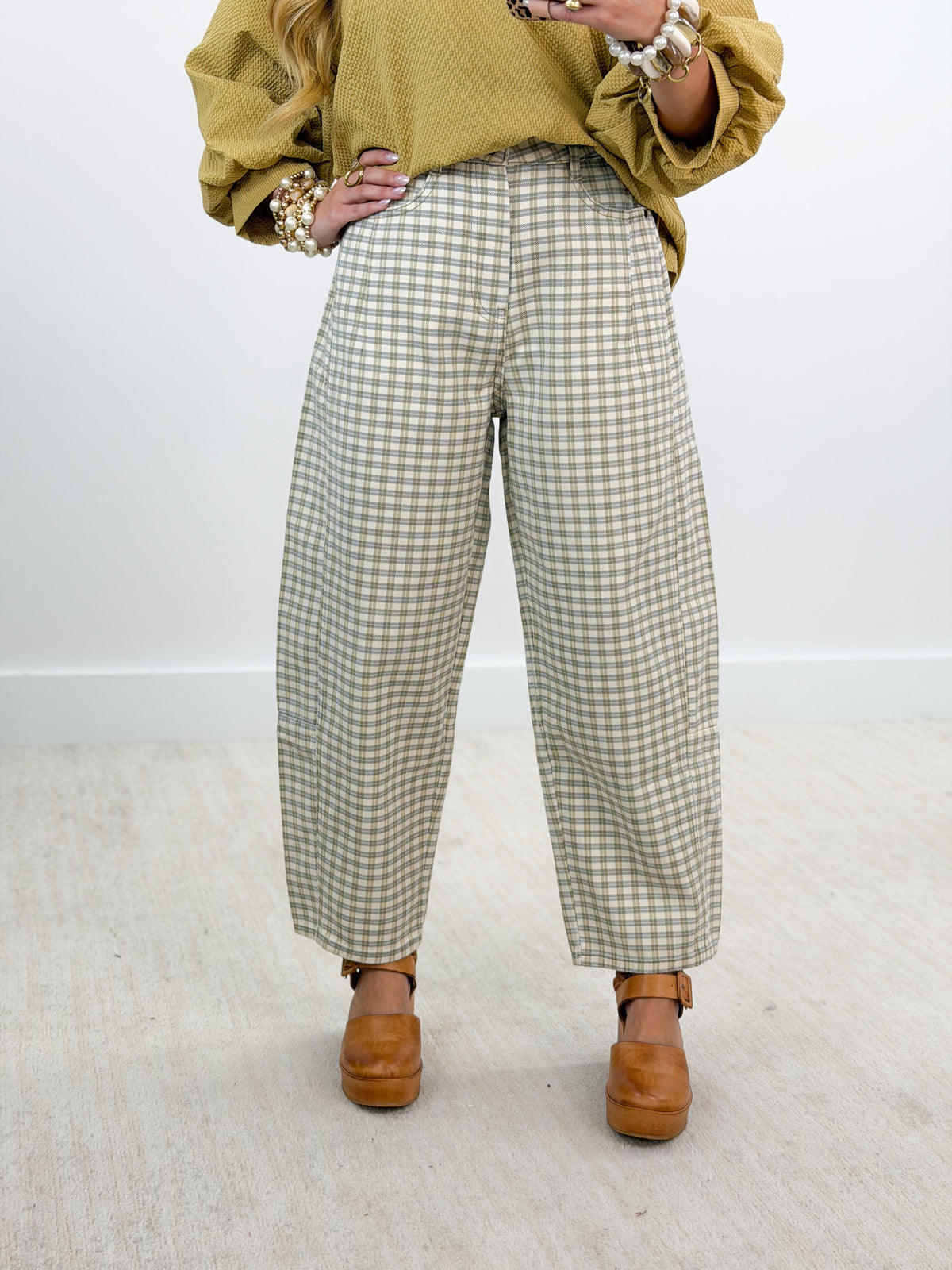 A person wearing wide-leg cropped trousers in a beige and white gingham pattern, styled with a mustard yellow top and brown platform shoes against a plain white wall and light floor.