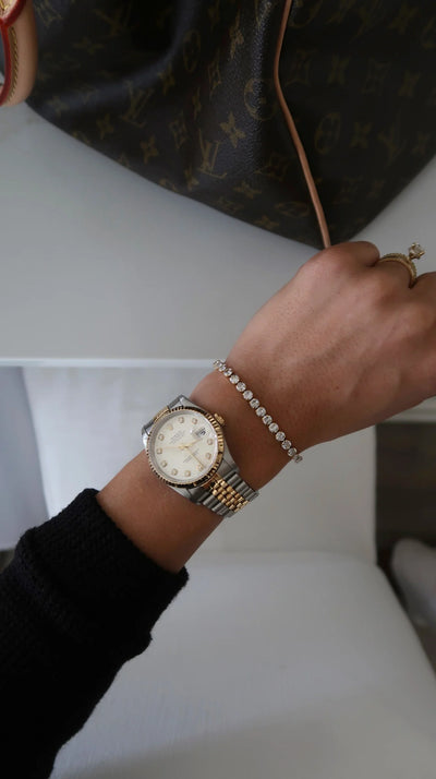 Person wearing a watch and bracelet on a white surface with a dark background