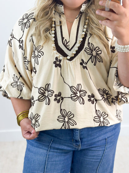 Ecru floral print collared V-neck blouse with black daisy pattern and beaded trim