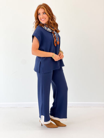 Side view of navy knit pants set with cuffed hems and white contrast trim