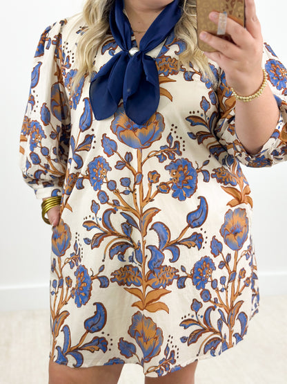 Ecru mini dress with blue and orange floral print, puff sleeves, navy tie-neck bow