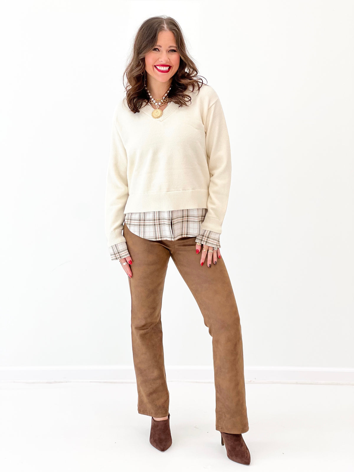 Cream knit V-neck sweater layered over plaid collared shirt hem