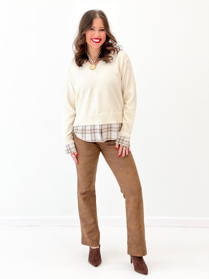 Cream knit V-neck sweater layered over plaid collared shirt hem