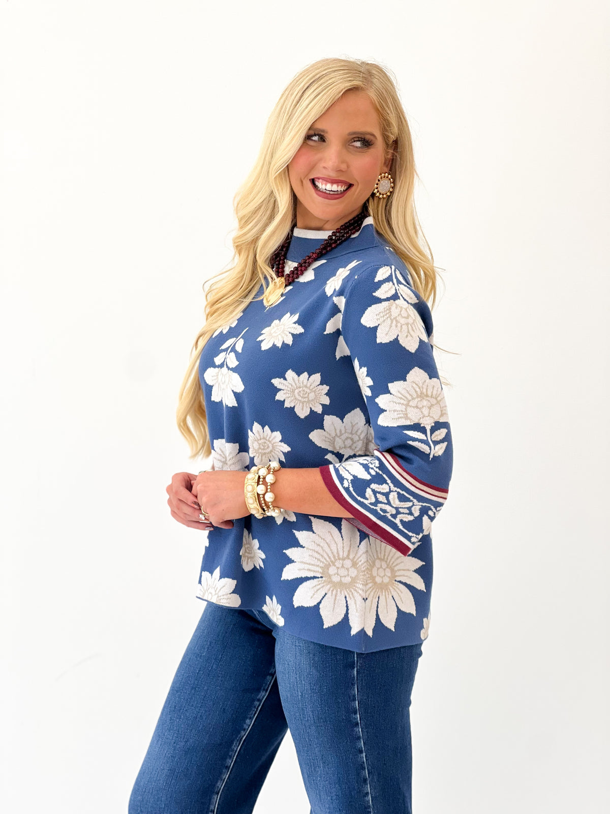 Blue mock neck knit sweater with white floral pattern and red-trim sleeve border