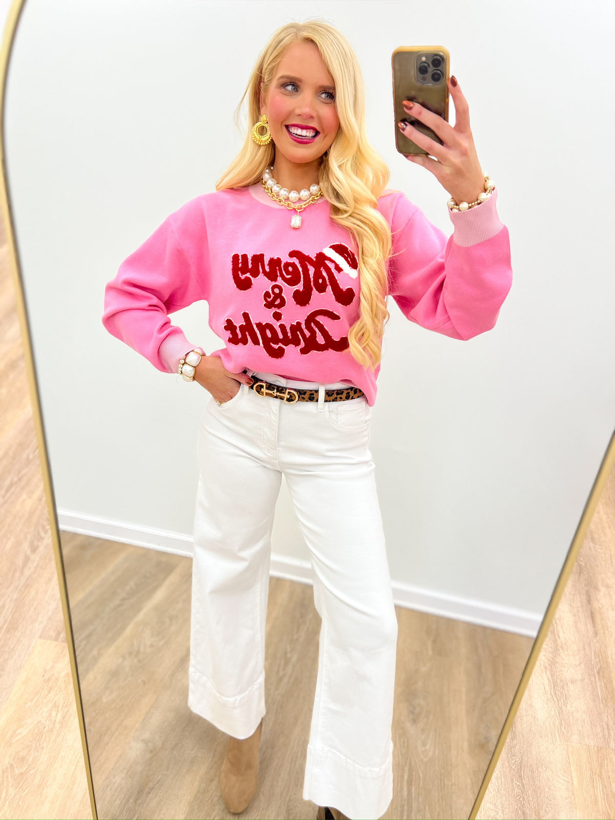 Pink crewneck sweater top with red Merry & Bright lettering, worn with white jeans