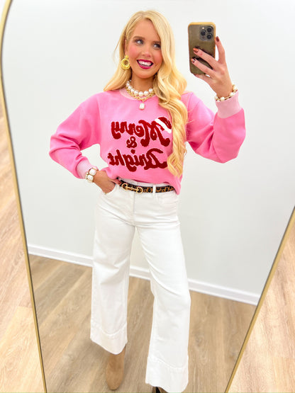Pink crewneck sweater top with red Merry & Bright lettering, worn with white jeans