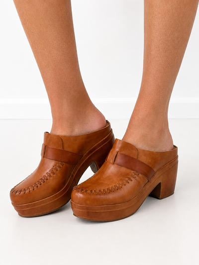 A pair of women's platform clogs in tan leather, shown on a model's feet against a clean white background.