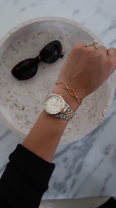 Hand wearing a watch with a bracelet, sunglasses in a bowl in the background