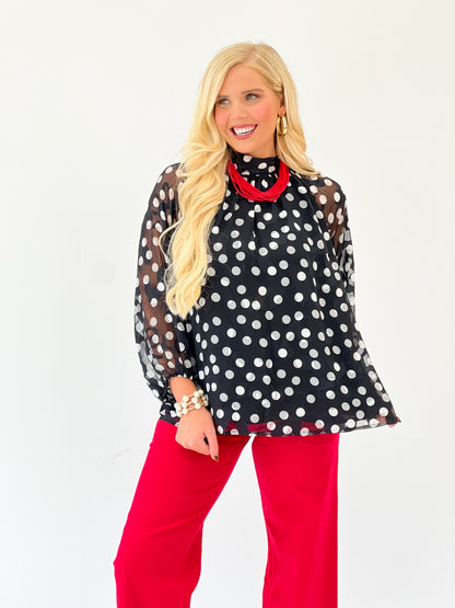 Black polka dot high-neck long-sleeve blouse with red contrast collar and cuffs