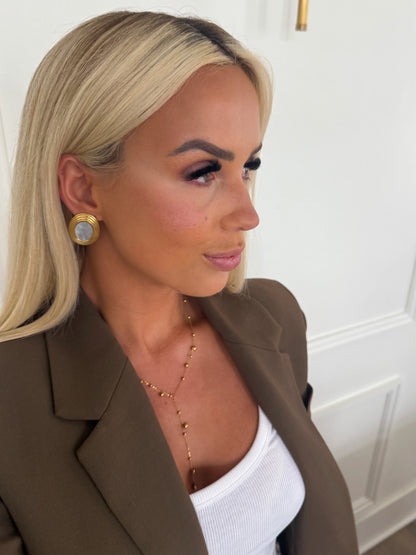 Gold-tone round hoop earrings with white mother-of-pearl inset, worn at ear