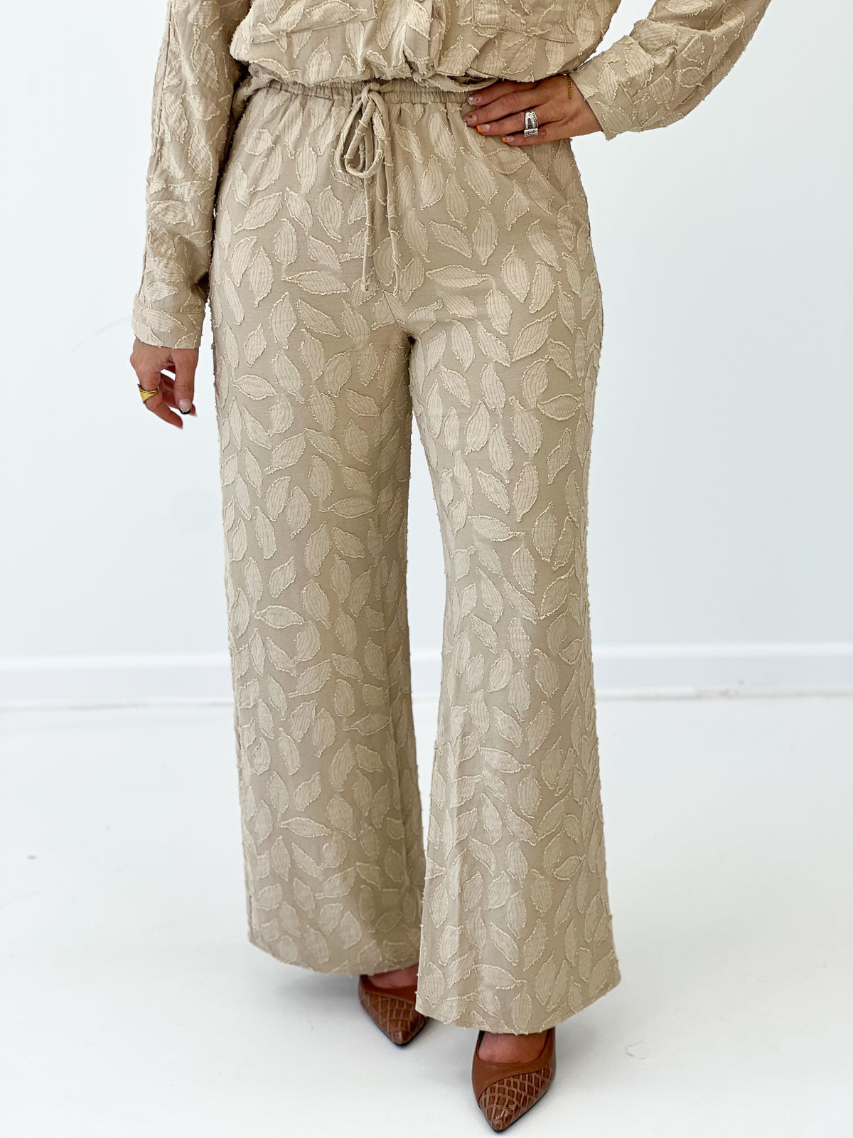 Taupe elastic tie-waist wide-leg pants with drawstring and leaf print detail.