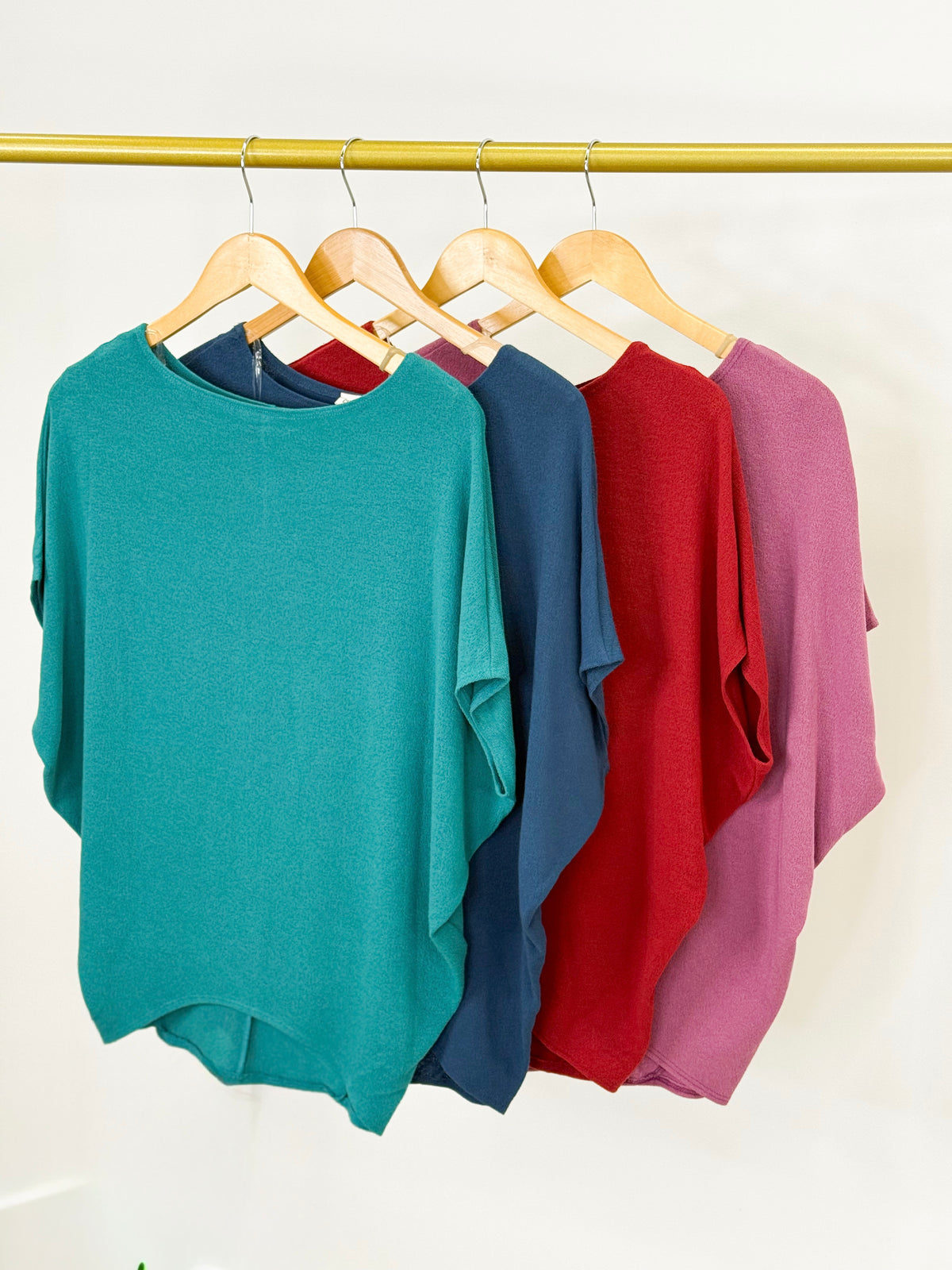 Short-sleeve dolman tops in teal, navy, red, and plum on hangers
