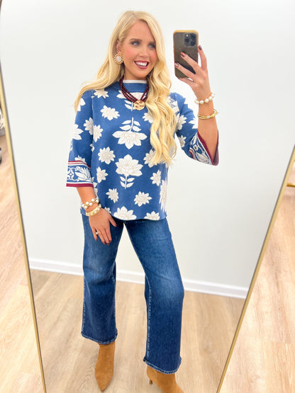 Blue mock neck knit sweater with white floral print and red-trimmed cuffs
