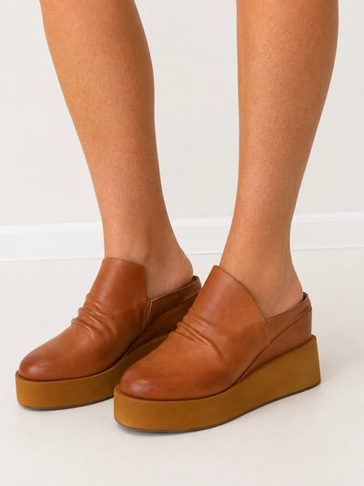 Tan leather platform mules worn with ankle-high pants