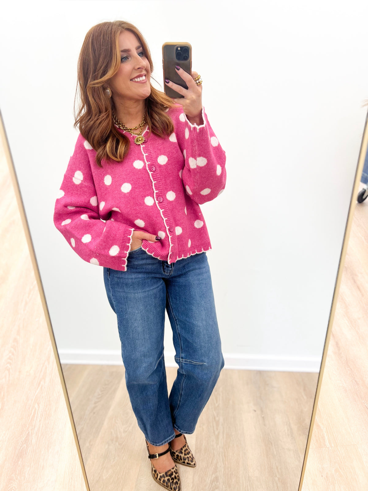 Pink polka dot button-front cardigan with long sleeves and scalloped trim.