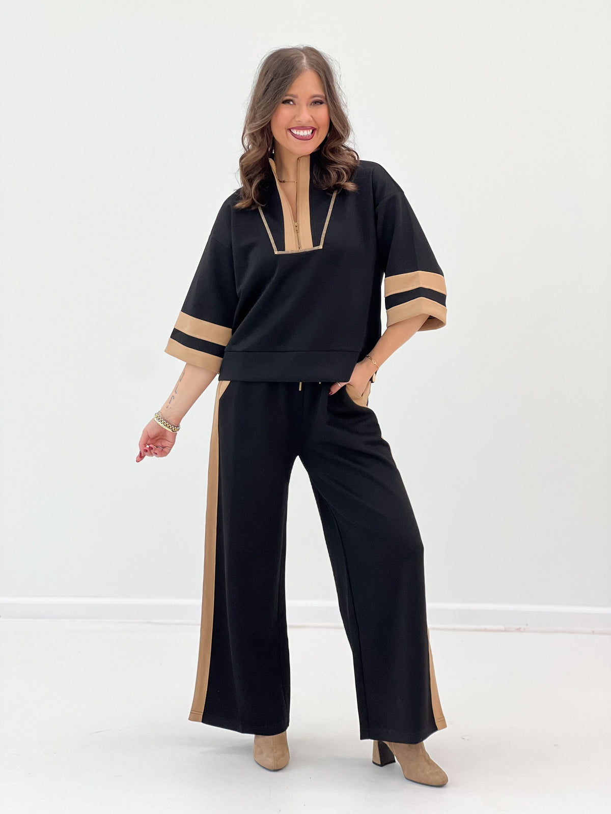 Black zip-up sweatshirt set with tan V-neck and sleeve stripe, paired with wide-leg pants