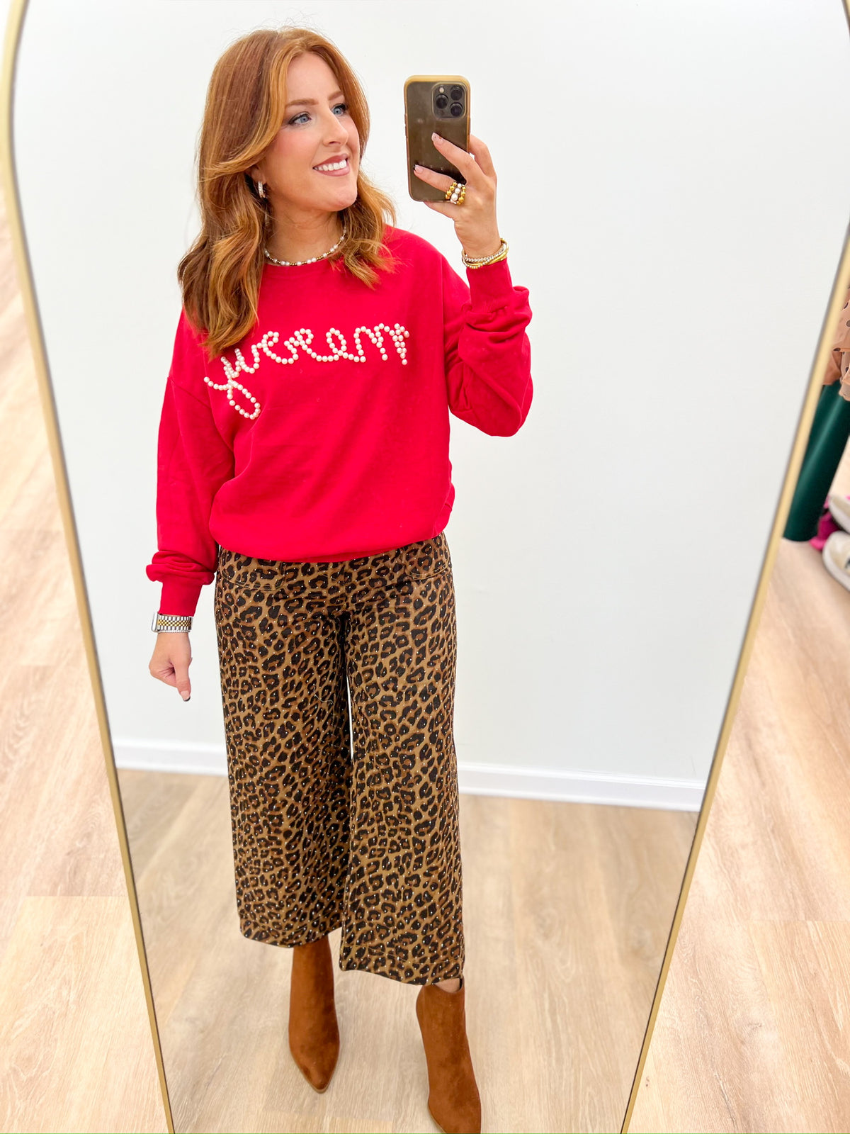 Red crewneck sweatshirt with pearl 'merry' script, shown from a side angle.