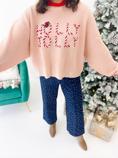 Light pink knit sweater close-up with red embroidered lettering, ribbed sleeves, cropped hem