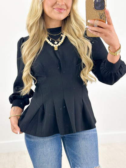 Black pleated flare top with ribbed knit trim at neckline and cuffs