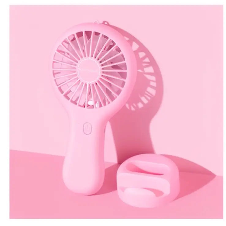 Pink portable handheld fan with a round grille, power button, and matching charging base