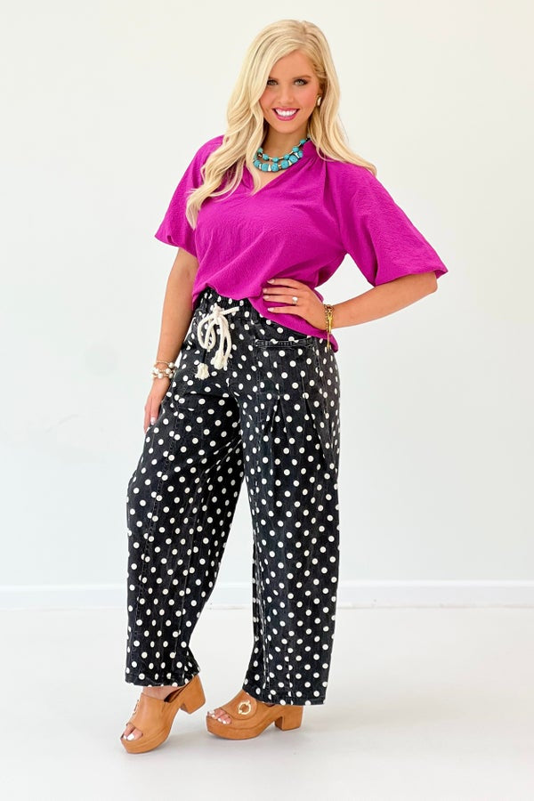 Woman wearing a bright pink top and black polka dot pants on a white background
