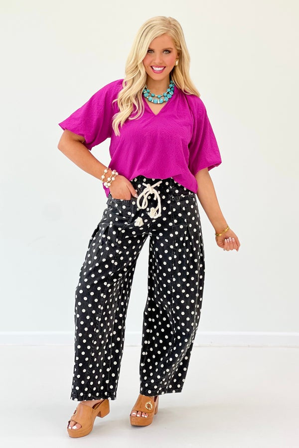Woman wearing a bright pink top and black polka dot pants on a white background
