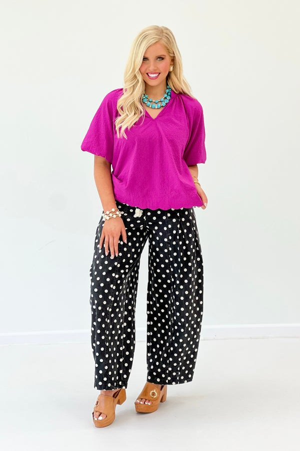 Woman wearing a bright pink top and black polka dot pants on a white background