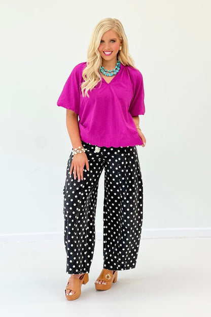 Woman wearing a bright pink top and black polka dot pants on a white background