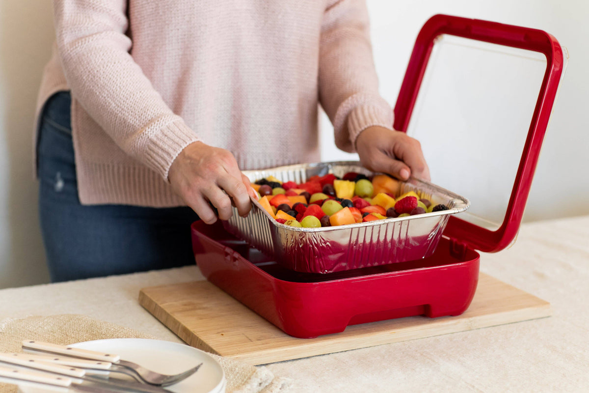 Red foil pan carrier with clear foil pan loaded with food, lid open