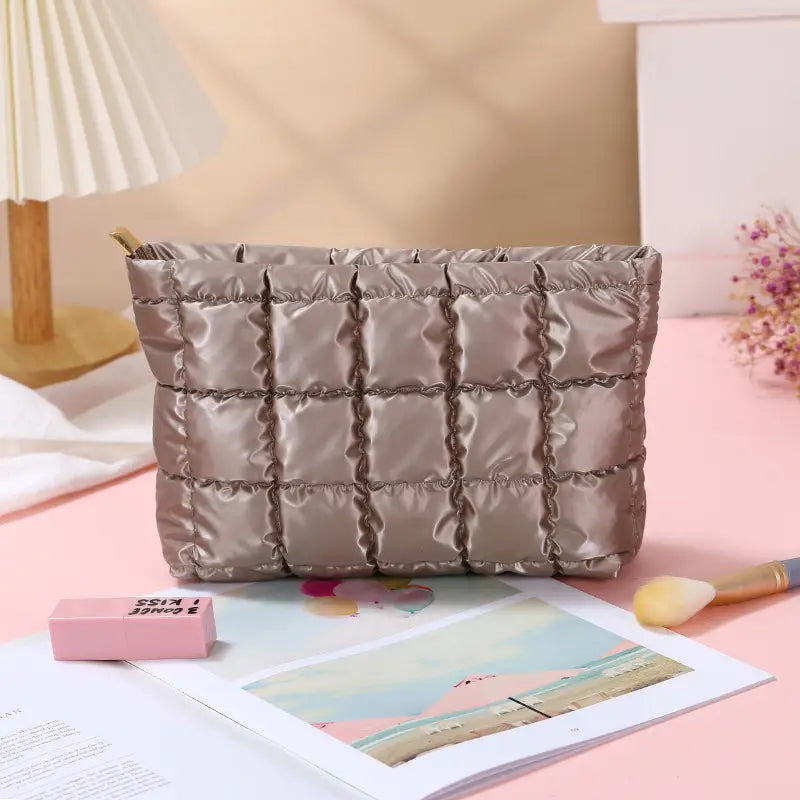 Small travel makeup bag in brown with a quilted, padded finish and zip closure.